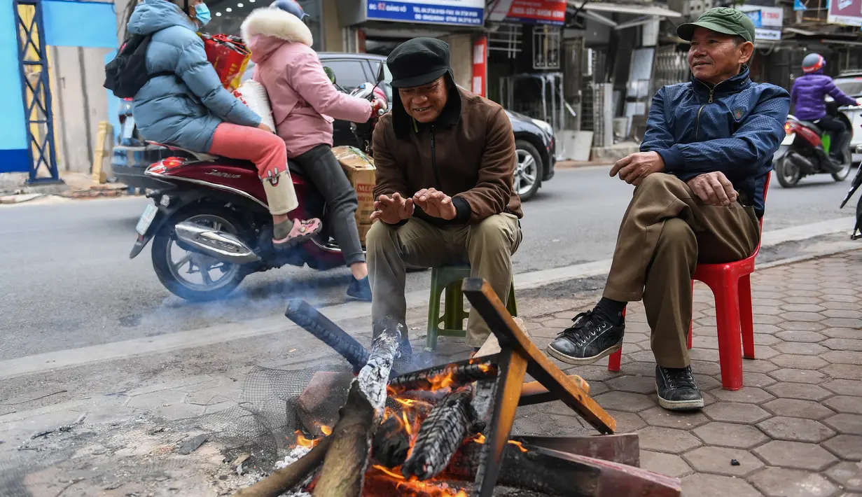 Orang-orang menghangatkan diri dengan membakar kayu pada hari musim dingin di Hanoi, Vietnam, Jumat (8/1/2021). Vietnam tahun ini diperkirakan mengalami musim dingin yang lebih dingin dari biasanya ketika suhu permukaan laut Samudra Pasifik turun, membentuk fenomena La Nina. (Nhac NGUYEN/AFP)