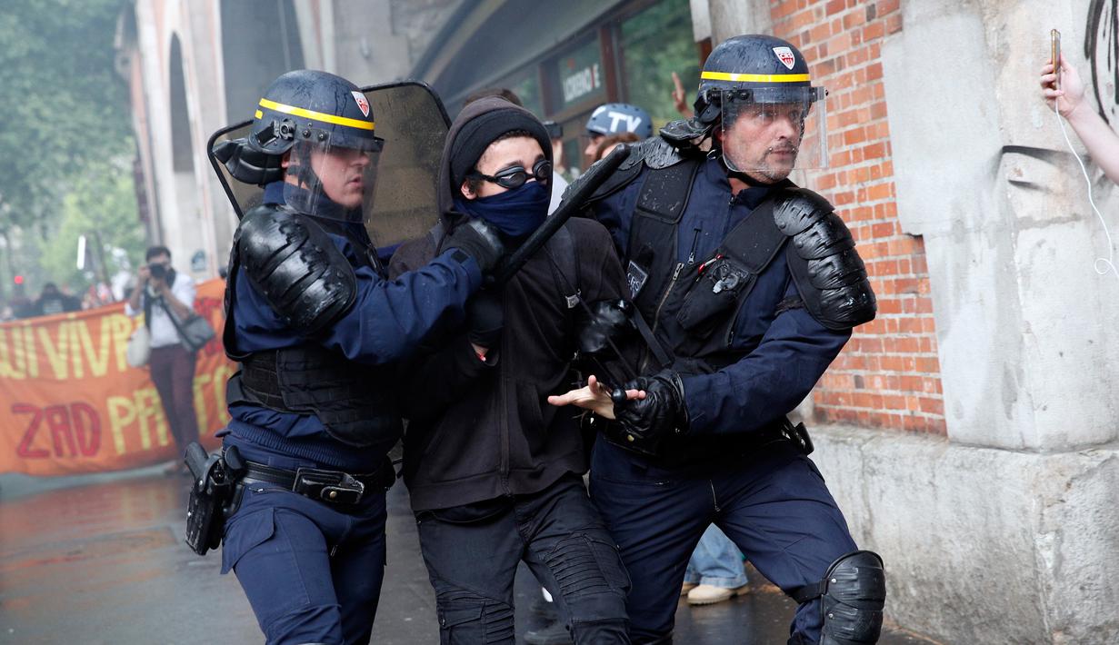 Polisi anti huru-hara mengamankan seorang demonstran saat terjadi bentrokan di Paris, Prancis (23/5). Mereka memprotes kebijakan pemerintah terkait pemangkasan 120.000 pekerjaan pada 2022. (AP/Christophe Ena)