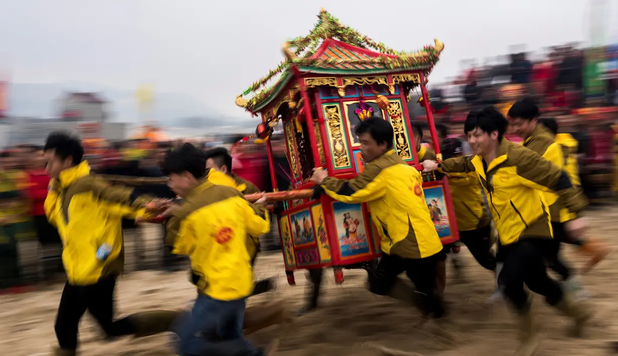 Penduduk desa membawa kuil Dewa Laut saat melakukan ritual di pantai desa Fuye, Provinsi Fujian, Tiongkok (5/3). Mereka adalah komunitas nelayan setempat yang menggelar ritual kepercayaan. (AFP Photo/Johannes Eisele)