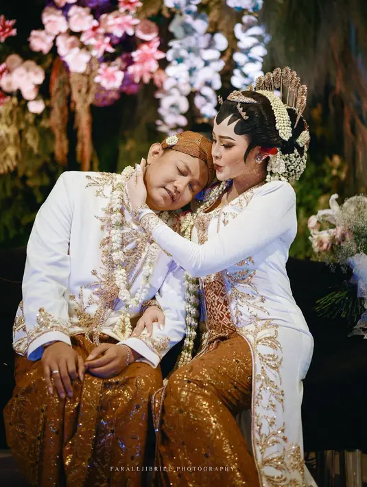 Denny Caknan tampil bak raja Jawa mengenakan beskap lengan panjang berwarna putih. Beskap ini diperindah dengan payet emas berbentuk daun yang membuat nuansa penampilannya secara keseluruhan terlihat semakin mewah. Foto: Instagram.