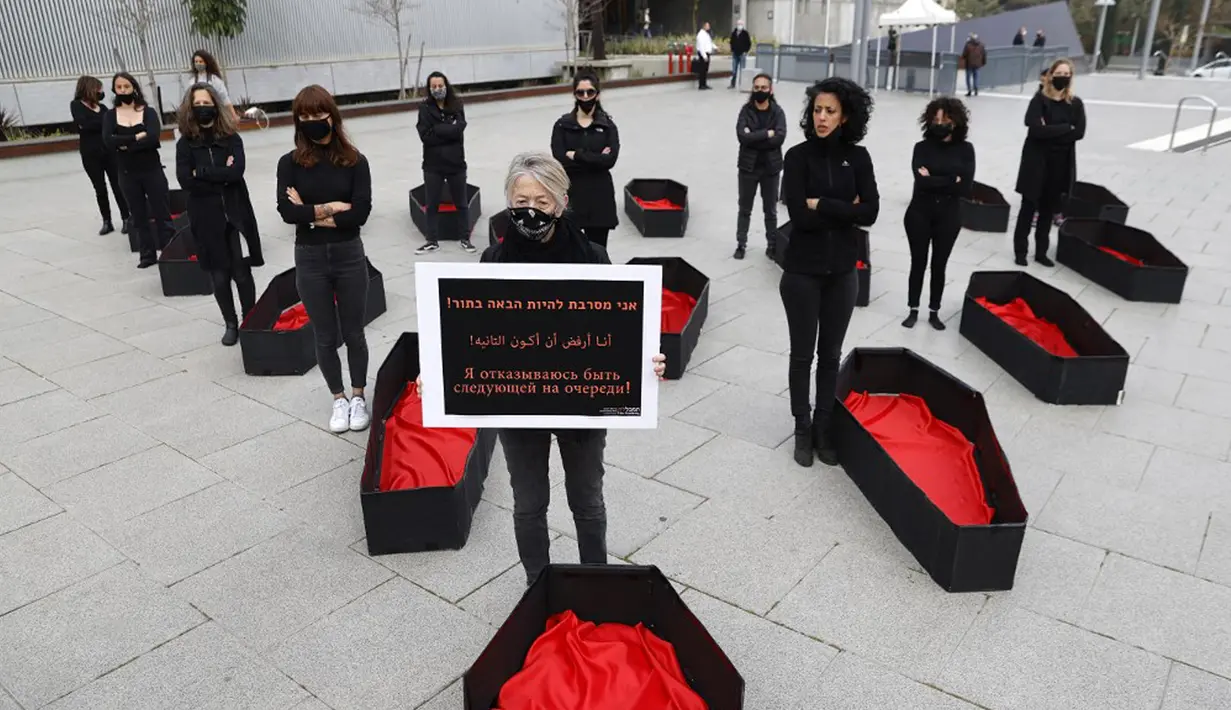 Seorang wanita memegang plakat bertulis "Saya menolak menjadi yang berikutnya" saat lainnya berdiri di samping peti mati tiruan mewakili yang tewas akibat kekerasan dalam rumah tangga jelang Hari Perempuan Internasional di luar Pengadilan Distrik, Tel Aviv, Israel, Minggu (7/3/2021). (JACK GUEZ/AFP)