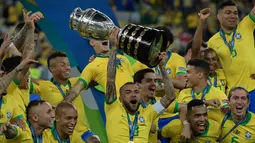 Pemain belakang timnas Brasil, Dani Alves mengangkat trofi Copa America 2019 saat berselebrasi bersama rekan setimnya setelah mengalahkan Peru pada partai final di Maracana Stadium, Rio de Janeiro, Senin (8/7/2019) dini hari WIB. Brasil menundukkan Peru dengan skor 3-1. (Juan MABROMATA/AFP)