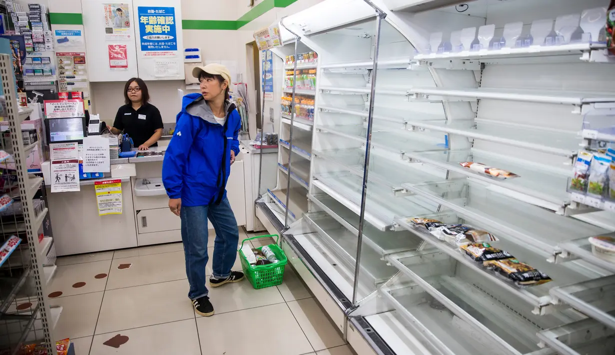 Rak-rak kosong terlihat saat pengunjung membeli  kebutuhan  di sebuah toko, distrik Shinagawa, Tokyo, Sabtu (12/10/2019). Banyak toko-toko perbelanjaan di Jepang yang kehabisan makanan dan minuman akibat warganya yang menimbun makanan untuk menghadapi topan Hagibis. (Odd ANDERSEN / AFP)