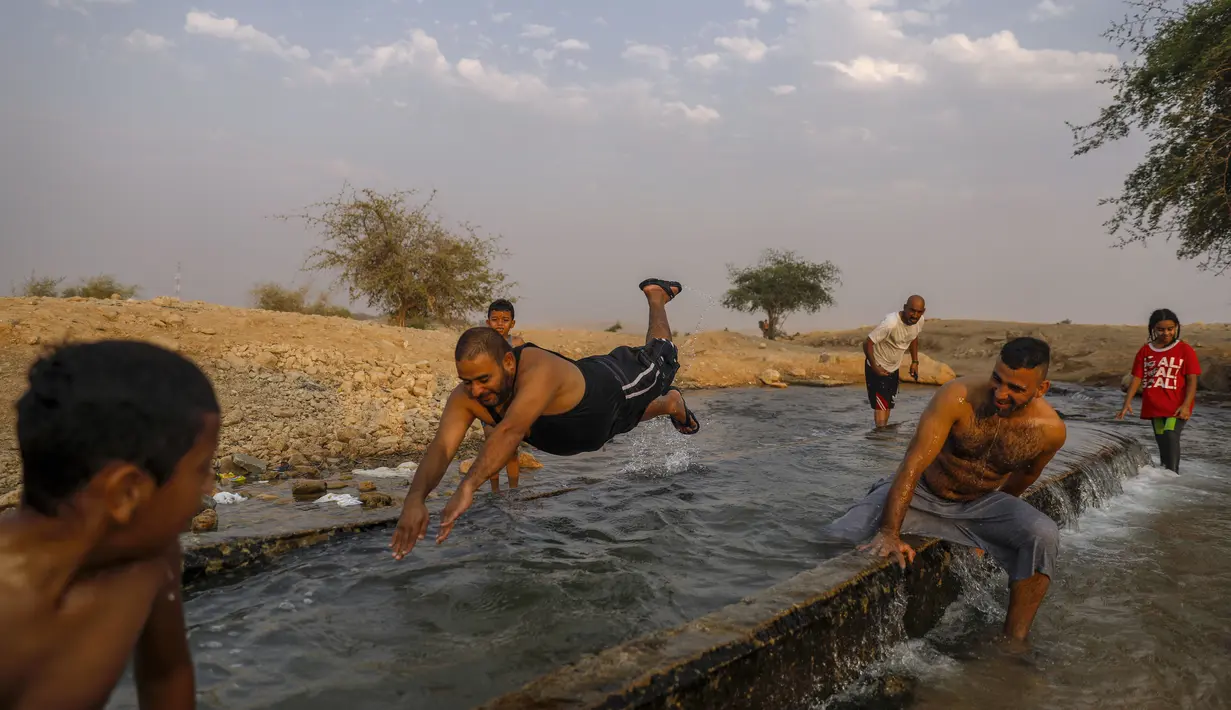 Warga Palestina meluncur di kanal air yang digunakan untuk irigasi untuk mendinginkan tubuh saat suhu udara mencapai 44 derajat Celcius di kota Jericho, Tepi Barat (1/9/2020). (AFP Photo/Ahmad Gharabli)