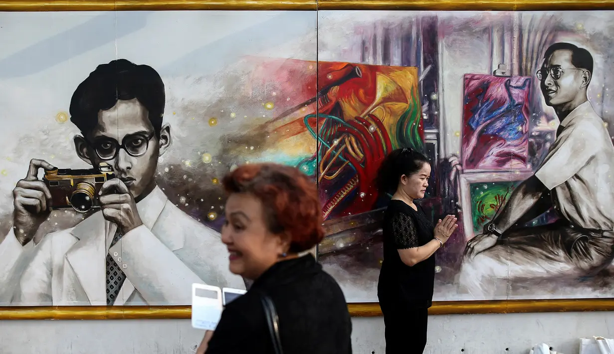 Warga yang melayat berdiri di depan gambar raja Thailand Bhumibol Adulyadej di dekat Grand Palace, Bangkok, Selasa (18/10). Lukisan yang dibuat mahasiswa seni dipajang di dekat Grand Palace di Bangkok, Thailand (18/10). (Reuters/Athit Perawongmetha)