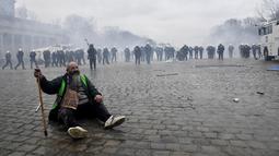 Seorang pria duduk di trotoar saat polisi menghadapi pengunjuk rasa yang menentang tindakan COVID-19 di Brussel, Minggu (23/1/2022). Pengunjuk rasa juga mengkritik kebijakan wajib vaksin untuk beraktivitas di tempat umum maupun mengikuti kegiatan tertentu. (AP Photo/Geert Vanden Wijngaert)