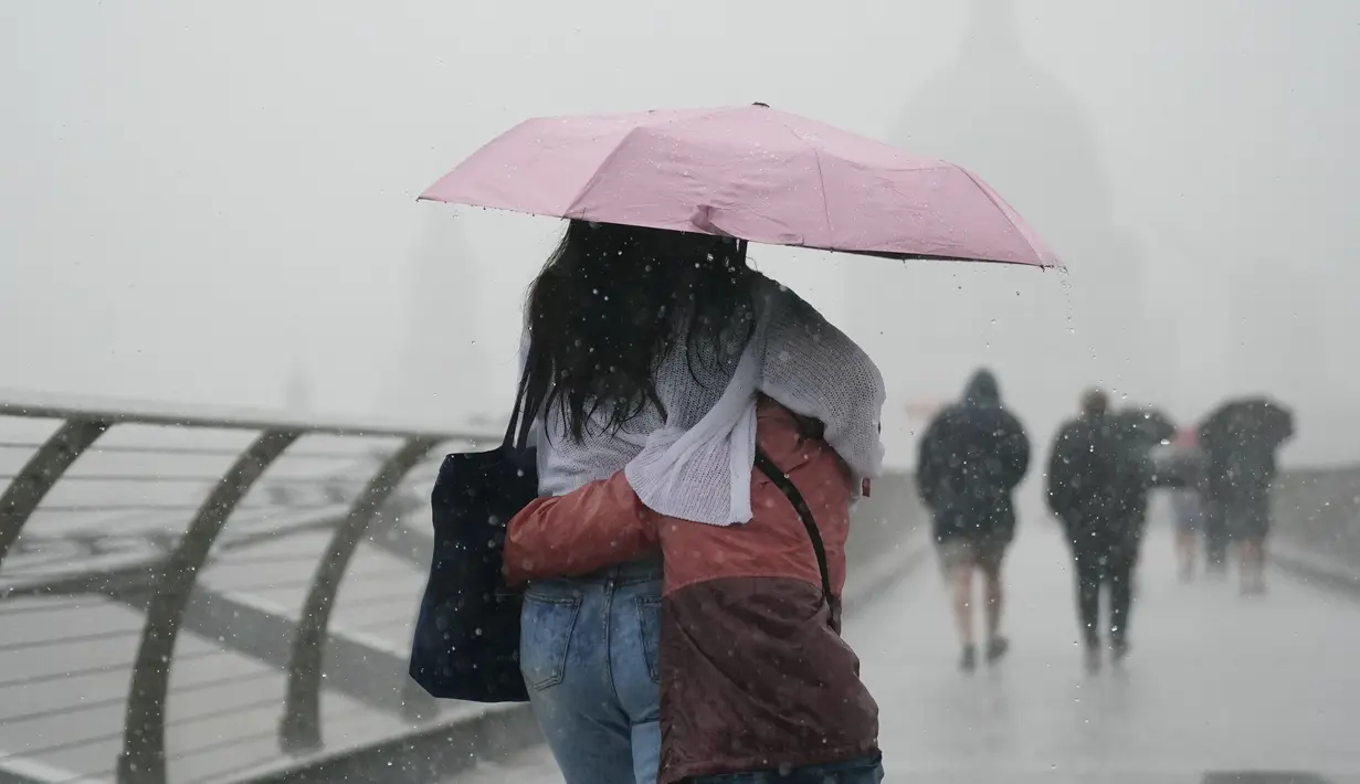 <p>Orang-orang dengan payung berjalan di tengah hujan di Jembatan Milenium, London, Rabu (17/8/2022). Setelah berminggu-minggu cuaca terik, yang telah menyebabkan kekeringan dan membuat tanah kering, peringatan badai petir kuning dari Kantor Meteorologi memperkirakan hujan lebat dan badai petir yang bisa melanda bagian Inggris dan Wales. (Victoria Jones/PA via AP)</p>