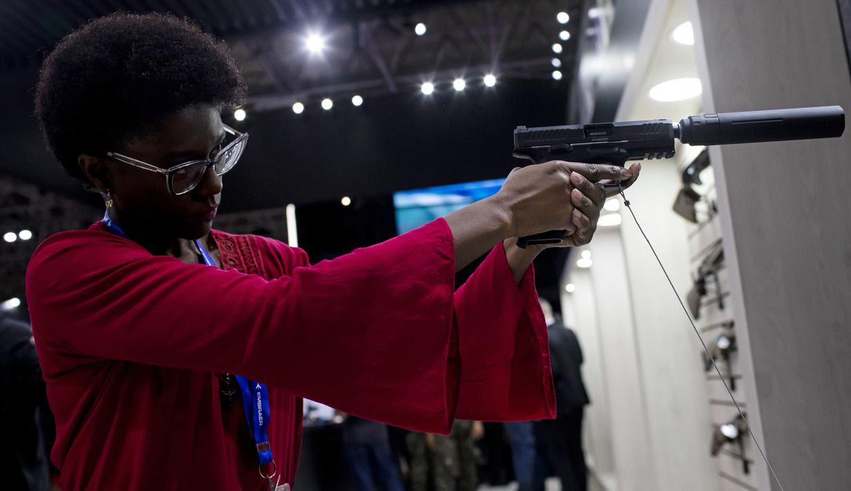 Seorang wanita memegang pistol dengan peredam di Pameran Internasional Pertahanan dan Keamanan LAAD di Rio de Janeiro, Brasil, Selasa, 11 April 2023. (AP Photo/Bruna Prado)