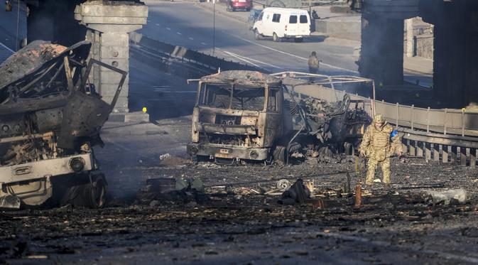 Seorang tentara Ukraina berjalan melewati truk militer yang terbakar, di sebuah jalan di Kiev, Ukraina, Sabtu (26/2/2022). Pasukan Rusia menyerbu ke arah ibu kota Ukraina pada Sabtu (26/2), dan pertempuran jalanan pecah saat pejabat kota mendesak penduduk untuk berlindung. (AP Photo/Efrem Lukatsky)