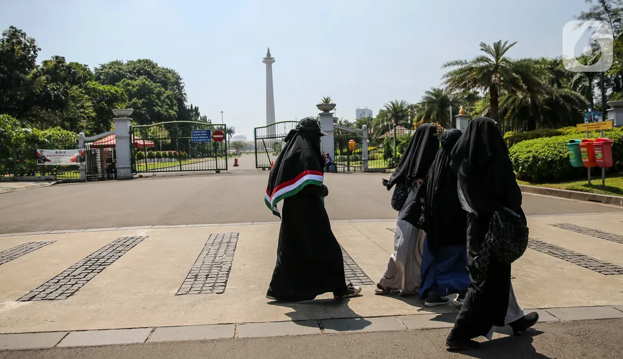 Sejumlah warga berjalan di depan kawasan Monumen Nasional (Monas), Jakarta, Minggu (26/7/2020). Sejumlah warga mulai mengunjungi kawasan Monas meski masih ditutup sementara di masa PSBB transisi. (Liputan6.com/Faizal Fanani)