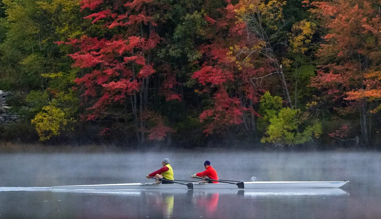 Sepasang pendayung meluncur di Sungai Androscoggin di Brunswick, Maine, tempat dedaunan berubah menjadi warna musim gugur, pada 10 Oktober 2021. Salah satu yang paling khas dari musim gugur adalah pohon-pohon yang berubah warna sebelum gugur. (AP Photo/Robert F. Bukaty)
