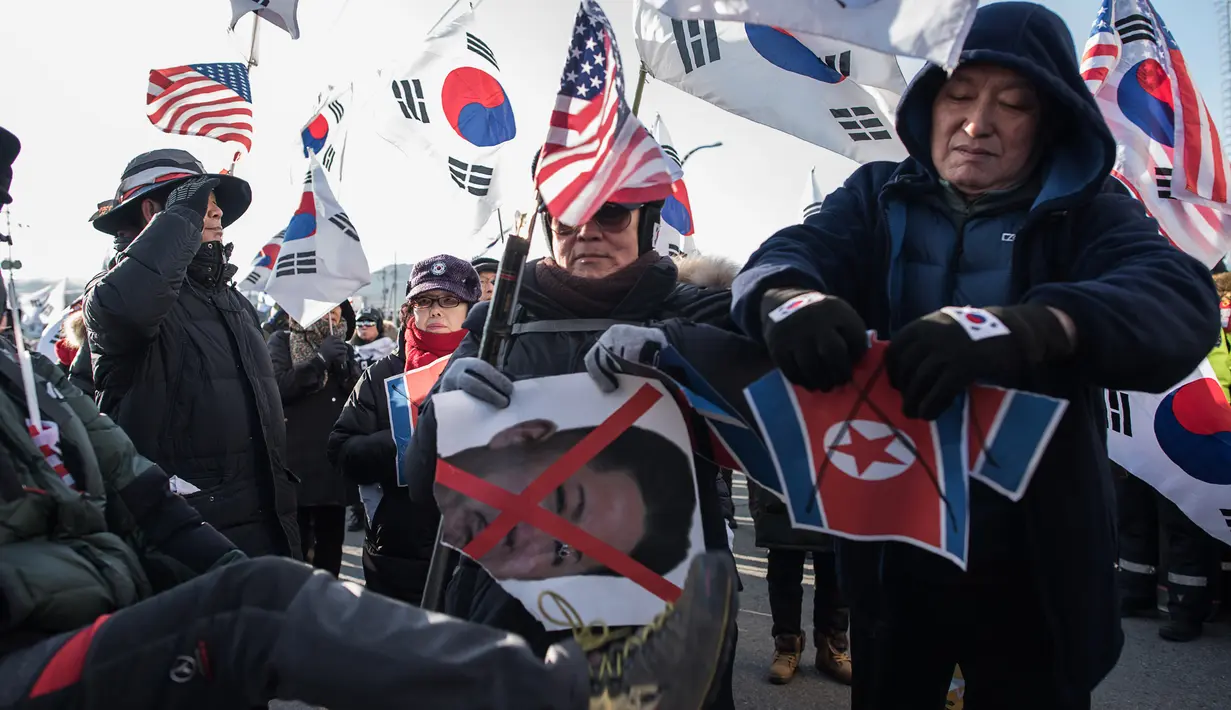 Pengunjuk rasa anti-Korea Utara merobek bendera Korea Utara saat melakukan aksi menyambut kedatangan kapal feri Korea Utara yang membawa rombongan seni untuk tampil di Olimpiade Musim Dingin Pyeongchang 2018, Korea Selatan (6/2). (AFP/Ed Jones)