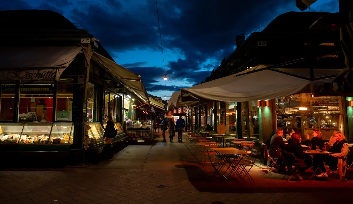 Orang-orang minum di pasar Naschmark yang biasanya penuh sesak di Wina, Austria pada 5 Oktober 2020. Naschmarkt adalah pasar tertua, terbesar, dan terpopuler di Wina kini sepi pengunjung akibat pandemi corona COVID-19. (JOE KLAMAR / AFP)