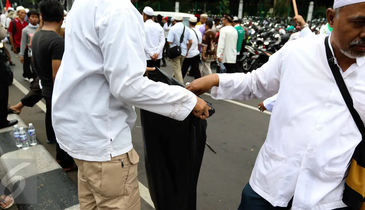 Massa membuang sampah ke kantong plastik yang disediakan oleh relawan di tengah aksi damai 4 November di Jakarta, Jumat (4/11). Mereka mengumpulkan sampah berupa bekas botol minuman dan bungkus nasi yang dibuang anggota ormas (Liputan6.com/Faizal Fanani)