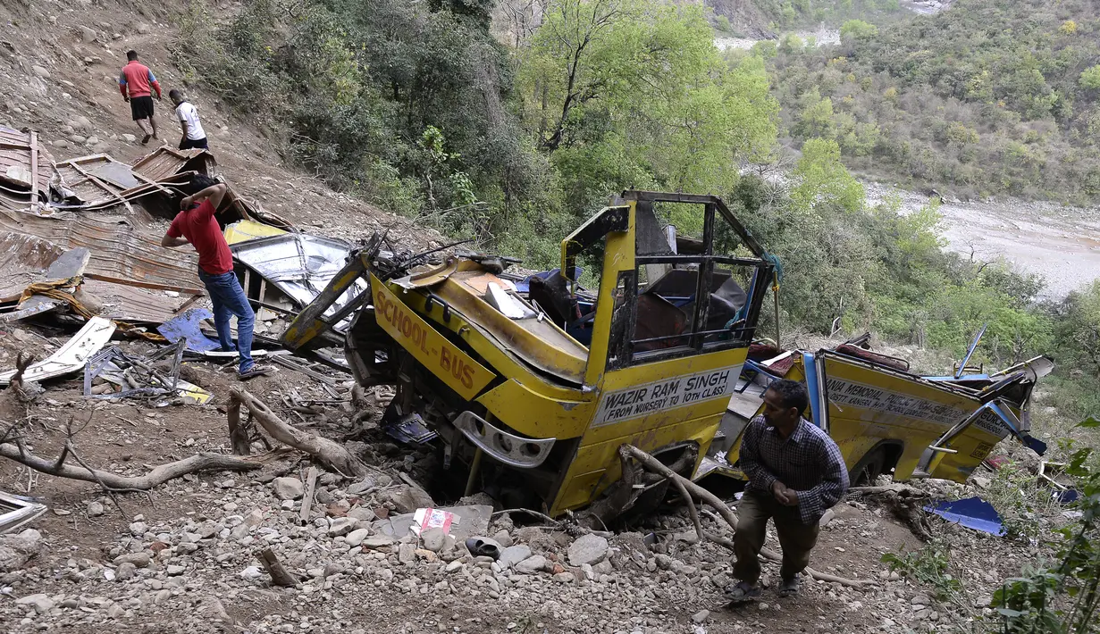 Warga melihat-lihat bangkai bus sekolah yang rusak akibat masuk jurang di dekat Nurpur, Distrik Kangra, Himachal Pradesh, India, Selasa (10/4). Menurut polisi, sebagian besar penumpang adalah pelajar berusia di bawah 10 tahun. (SHAMMI MEHRA/AFP)