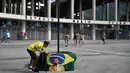 <p>Seorang pria memasang bendera Brasil dengan gambar mendiang legenda sepak bola Pele di bawah tanda jalan bertuliskan "Avenue King Pele" di luar stadion Maracana di Rio de Janeiro, Brasil pada 4 Januari 2023. Balai Kota Rio de Janeiro secara resmi menamai jalan yang mengelilingi stadion Maracana Avenue Rei Pele (King Pele). (MAURO PIMENTEL/AFP)</p>