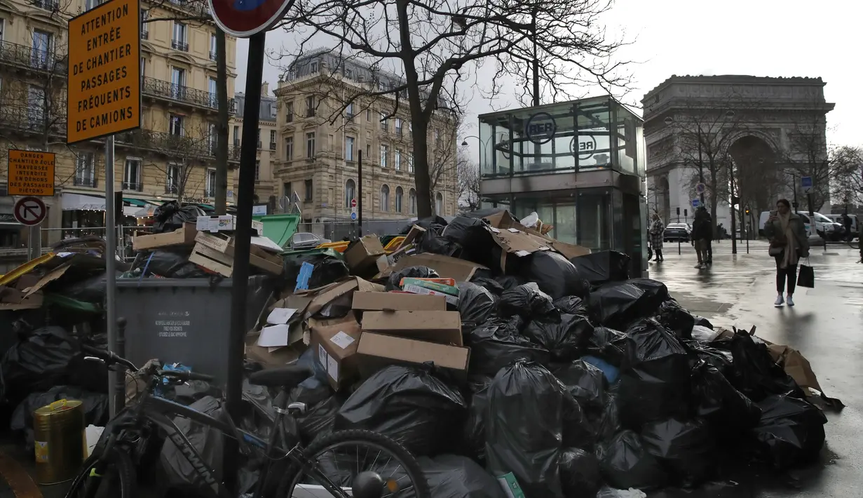 Orang-orang berjalan melewati tumpukan kantong sampah di Paris (4/2/2020). Sampah menumpuk di jalan-jalan Paris dan Marseille karena pemogokan perubahan pada sistem pensiun nasional Prancis.  (AP Photo/Christophe Ena)