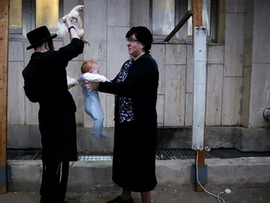 Seorang pria Yahudi Ultra-Ortodoks memegang ayam di atas kepala bayi saat melakukan ritual Kaparot, di Ashdod, Israel, (9/10). Dalam ritual ini ayam putih disembelih sebagai syarat simbolis dari penebusan. (REUTERS/Amir Cohen)