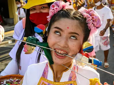 Seorang wanita menusuk pipinya dengan besi  saat mengikuti prosesi perayaan Festival Vegetarian tahunan di Phuket, Thailand, Kamis (3/10/2019). Festival ini biasanya berlangsung selama 9 hari di akhir September sampai Oktober. (AFP Photo/Mladen Antonov)