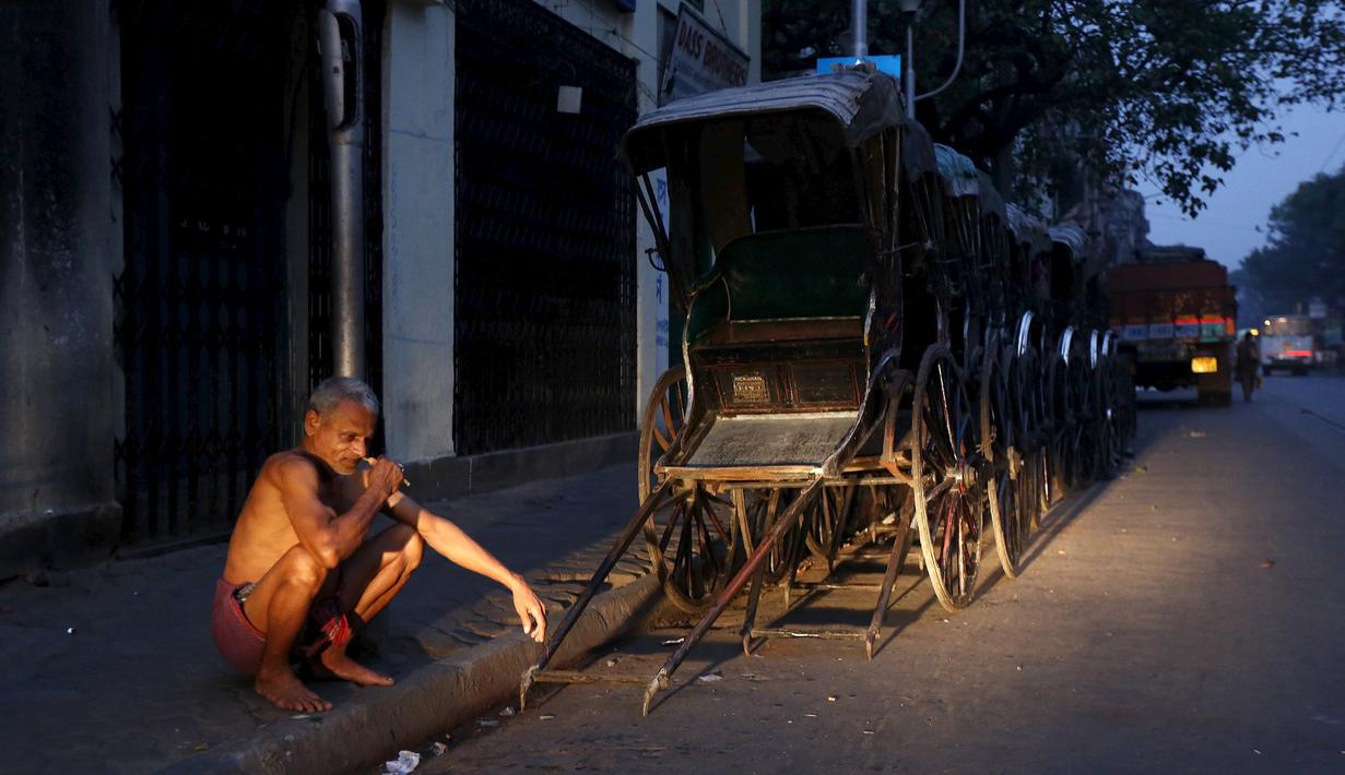 Seorang pria sikat gigi dengan ranting neem di samping deretan becak di Kolkata, 12 Maret 2016. Badan Pusat Statistik India mencatat sebanyak 360 juta rakyat di negeri itu hidup di bawah garis kemiskinan, salah satunya Kolkata (REUTERS/Rupak De Chowdhuri)