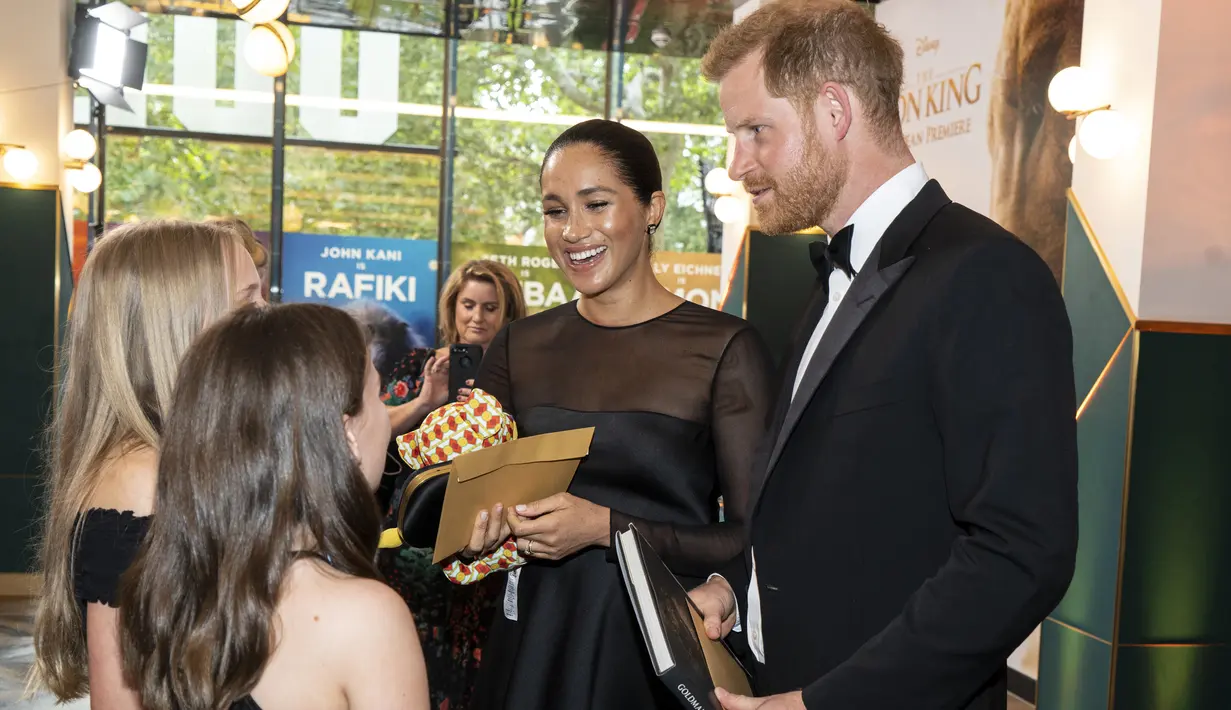 Pangeran Harry dan Meghan Markle berbincang dengan anak-anak muda eksekutif Disney saat tiba menghadiri pemutaran film The Lion King di London (14/7/2019). Duchess of Sussex tampil menawan dalam balutan gaun hitam dengan detail lebar di bagian bawah rok. (AFP Photo/Niklas Halle'n)