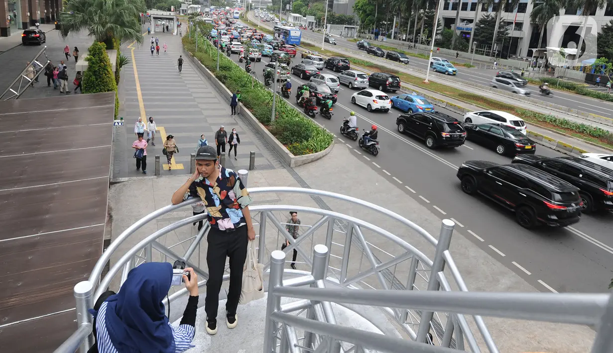 Warga berfoto di jembatan penyeberangan orang (JPO) yang tidak beratap di jalan Sudirman, Jakarta, Rabu (6/11/2019). Pemprov DKI mengklaim mayoritas masyarakat Jakarta setuju dengan konsep JPO terbuka dan tanpa atap yang kini dibangun di Sudirman. (merdeka.com/Arie Basuki)