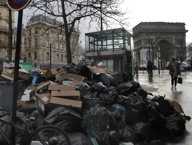 Orang-orang berjalan melewati tumpukan kantong sampah di Paris (4/2/2020). Sampah menumpuk di jalan-jalan Paris dan Marseille karena pemogokan perubahan pada sistem pensiun nasional Prancis.  (AP Photo/Christophe Ena)