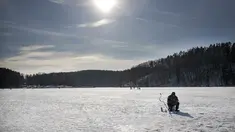 Seorang pria memancing melalui lubang es di danau beku yang tertutup salju dekat Vilnius, Lithuania, Minggu (13/2/2022). Suhu udara 0 derajat Celcius (32 derajat Fahrenheit). (AP Photo/Mindaugas Kulbis)