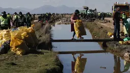 Relawan membawa kantong berisi sampah yang dikumpulkan dari Sungai Tagaret, yang mengalir ke Danau Uru Uru, dekat Oruro, Bolivia, Rabu (7/4/2021). Operasi pembersihan dimulai dalam upaya mengembalikan danau ke keindahan alamnya yang telah dibanjiri sampah plastik dan limbah lainnya. (AP/Juan Kari)