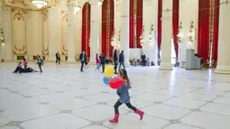 Seorang gadis kecil memegang balon berjalan melalui aula Istana Parlemen pada Hari Anak Internasional di Bucharest, Rumania, Selasa (1/6/2021). Orang-orang memanfaatkan kesempatan untuk mengunjunginya secara gratis. (AP Photo/Vadim Ghirda)