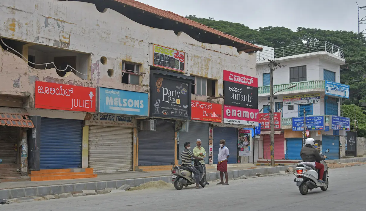 Orang-orang berdiri di depan pertokoan yang tutup di area komersial saat lockdown di Bangalore, Rabu (15/7/2020). Pusat IT India, Bangalore, kembali memberlakukan lockdown selama seminggu dimulai dari 14 Juli 2020 untuk menahan lonjakan kasus Covid-19 yang meningkat. (Manjunath Kiran/AFP)