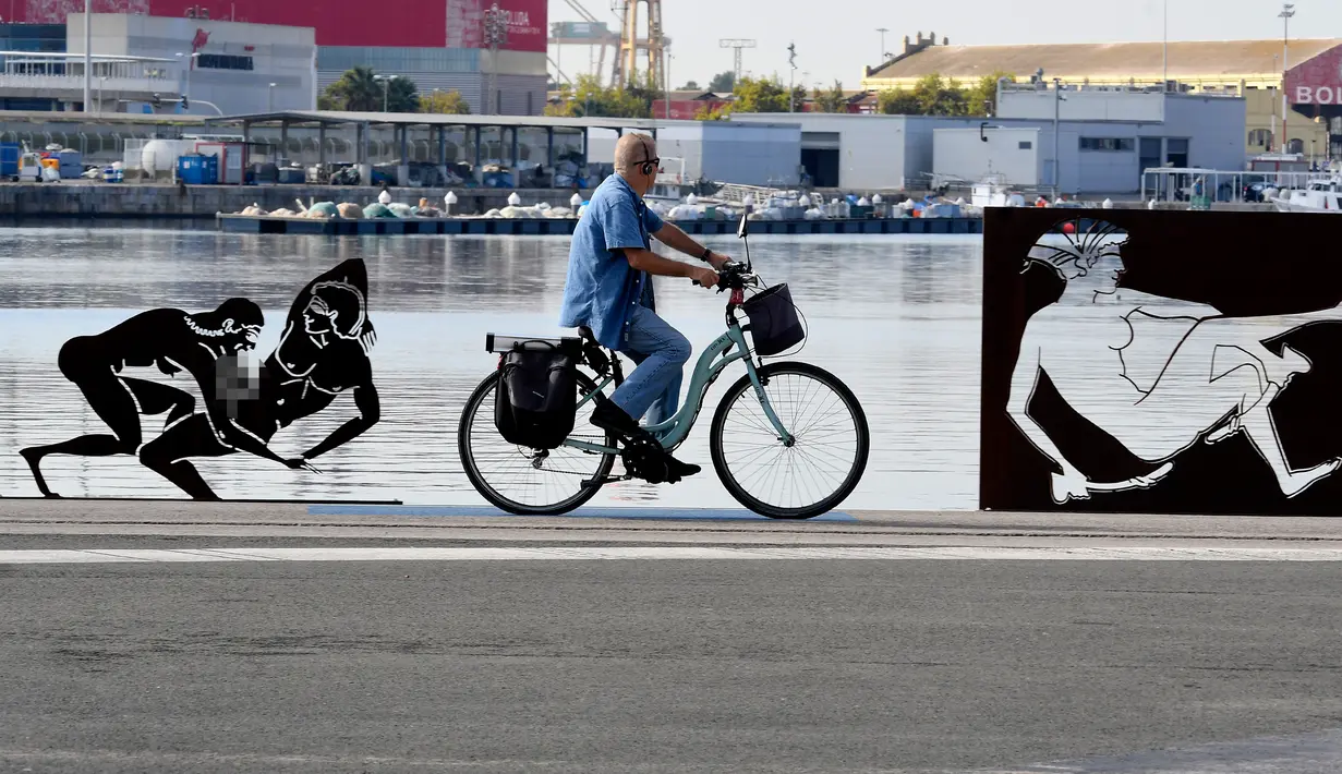 Pengendara sepeda melintas di samping patung erotis karya seniman Antoni Miro yang dipamerkan di pelabuhan Valencia, Spanyol (19/9). (AFP Photo/Jose Jordan)