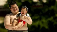 Seorang pegulat sumo amatir ikut menangis saat dia  menggendong bayi yang juga menangis di Tokyo, Jepang, (30/5/2015). Kontes ini merupakan kontes untuk suara bayi dengan tangis yang paling kencang. (REUTERS/Thomas Peter)