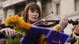 Anggota orkestra bermain sebagai bagian dari demonstrasi anti-perang menyusul serangan Rusia terhadap Ukraina di Trafalgar Square, London, Minggu (6/3/2022).  Flashmob yang terdiri dari 200 musisi klasik itu untuk menunjukkan dukungan terhadap Ukraina setelah invasi Rusia. (AP Photo/Alberto Pezzali)