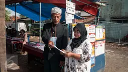 Petugas KPPS mengenakan pakaian adat dan belangkon memberikan pelayanan kepada warga yang menggunakan hak pilih di TPS 14 Cipinang Besar Selatan, Jakarta, Rabu (19/4). (Liputan6.com/Gempur M. Surya)