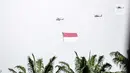Helikopter TNI AU mengibarkan bendera Merah Putih raksasa di kawasan Gedung DPR RI, Jakarta, Selasa (5/10/2021). TNI AU mengerahkan enam helikopter yang membawa bendera Merah Putih serta bendera Trimatra raksasa. (Liputan6.com/Faizal Fanani)