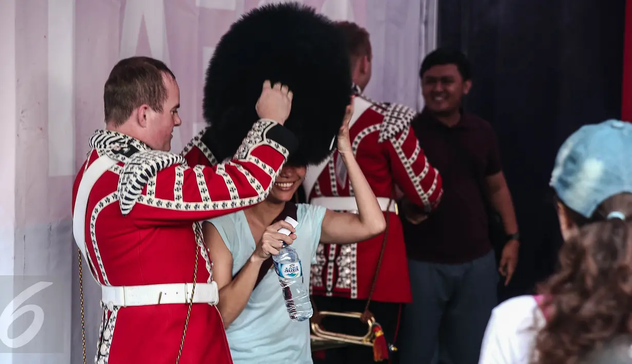 Seorang pasukan Scotts Guard alias penjaga Istana Inggris memakaikan topi berbulu ke warga yang ingin berselfie, usai beraksi di sela kegiatan Car Free Day (CFD) di kawasan Bundaran HI, Jakarta, Minggu (5/6). (Liputan6.com/Faizal Fanani)
