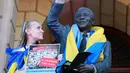 Katerina Kalinina dari Ukraina mengibarkan bendera negaranya pada patung mantan Presiden Afrika Selatan Nelson Mandela saat demonstrasi peringatan satu tahun invasi Rusia ke Ukraina di Balai Kota Cape Town, Afrika Selatan, 24 Februari 2023. (AP Photo/Nardus Engelbrecht)