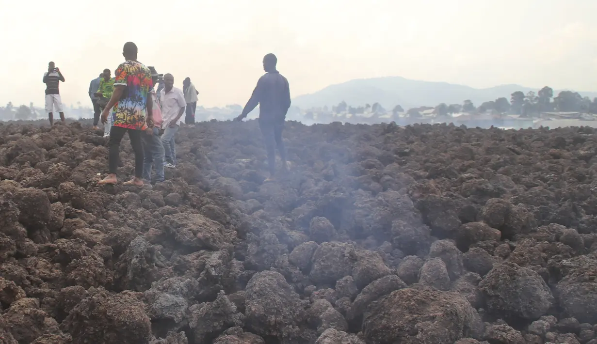 Warga memeriksa kerusakan akibat lahar dari letusan Gunung Nyiragongo semalam, terlihat di latar belakang, di Buhene, di pinggiran Goma, Kongo (23/5/2021). (AP Photo/Justin Kabumba)