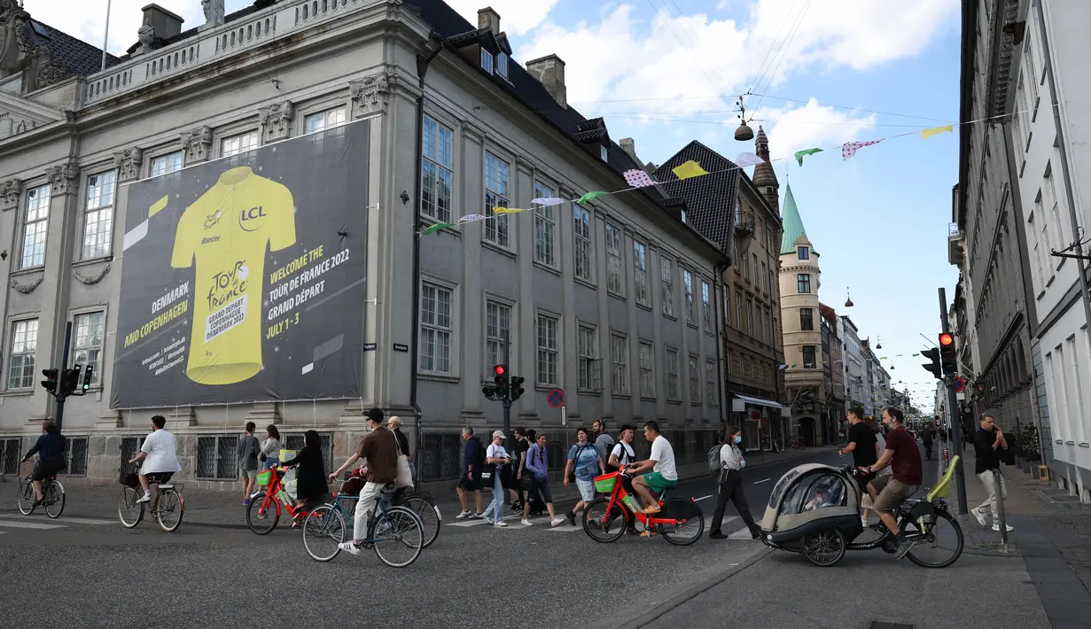 <p>Pengendara sepeda dan pejalan kaki melewati poster raksasa yang mengumumkan balapan sepeda Tour de France 2022 Grand Depart di Kopenhagen, Denmark pada 28 Juni 2022. Nuansa kuning menyambut kejuaraan balap sepeda legendaris, Tour de France (TdF), yang pada edisi 2022 akan bermula dari Kopenhagen. (Thomas SAMSON / AFP)</p>