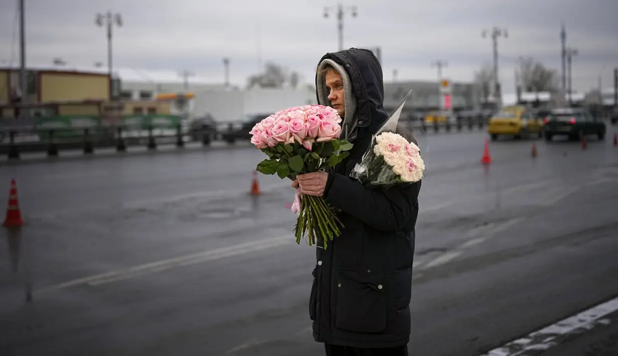 Seorang pria menunggu bus dengan buket bunga segar dari pasar bunga pada Hari Perempuan Internasional di Moskow, Rusia, 8 Maret 2022. (AP Photo)