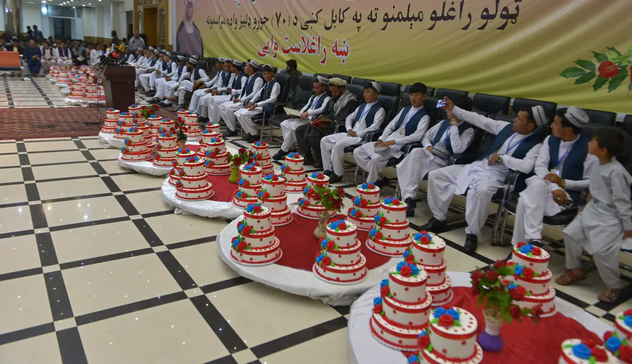 Para pengantin pria duduk dalam aula pernikahan saat mereka menunggu dimulainya upacara pernikahan massal di Kabul, Afghanistan, 13 Juni 2022. Upacara pernikahan dihadiri ratusan tamu dan pejuang Taliban yang membawa senjata. (Sahel ARMAN/AFP)