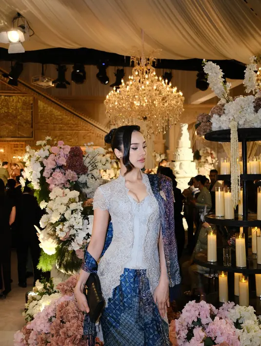 Kesan tradisional yang anggun semakin terasa lewat kain batik bernuansa biru navy dengan motif klasik yang dipadukan sebagai bawahan sekaligus selendang di salah satu sisi bahunya. Kombinasi warna silver dan biru gelap menciptakan harmoni yang elegan, membuat penampilan Anya terlihat berkelas di tengah dekorasi pesta pernikahan yang megah. [@anyageraldine].