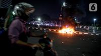 Polisi melintas dekat sejumlah barang yang terbakar usai demonstrasi berujung anarkis di kawasan Bundaran HI, Jakarta, Kamis (8/10/2020). Massa membakar sejumlah barang saat demonstrasi menolak pengesahan UU Cipta Kerja. (Liputan6.com/Faizal Fanani)