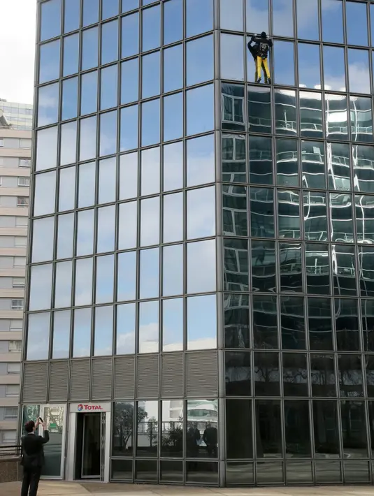 Seorang pria mengambil gambar aksi Alain Robert ketika memanjat gedung di pusat bisnis La Defense, Paris, Prancis, Senin (21/3/2016). Pria yang dijuluki 'Spiderman' ini telah memanjat lebih dari 70 gedung tertinggi di dunia. (Jacques DEMARTHON/AFP)