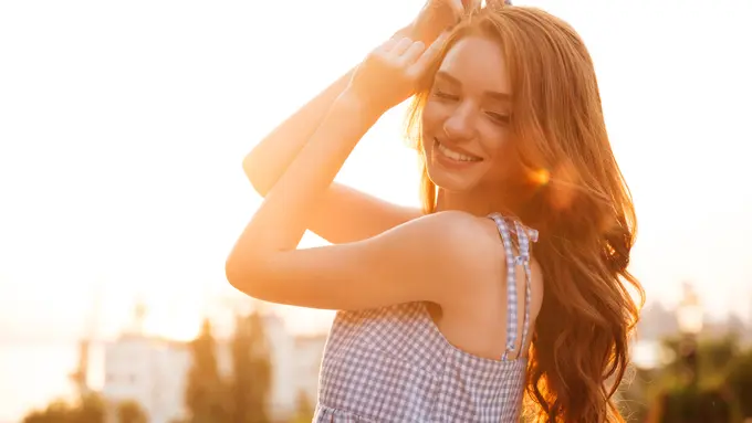 Seorang perempuan berpose mengangkat tangannya dengan disinari cahaya matahari (Foto Dok: Freepik/drobotdean)