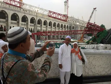 Calon jemaah haji foto bersama dengan latar berlakang crane yang roboh di Masjidil  Haram, Kota Mekah,  Arab Saudi (9/12/2015). Sebanyak 107 calon jemaah haji meninggal dunia akibat crane jatuh karena cuaca buruk. (AFP PHOTO / STR)