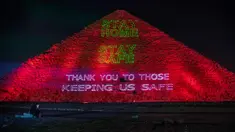 Seorang jurnalis melihat ponselnya ketika Kementerian Purbakala Mesir menyalakan piramida sebagai ungkapan dukungan bagi petugas kesehatan yang memerangi pandemi corona Covid-19 di Giza, Senin (30/3/2020). (AP/Nariman El-Mofty)