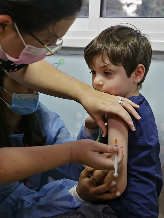 Bocah Israel, Itamar (5) disuntik dosis vaksin Covid-19 Pfizer/BioNTech Covid-19 di Meuhedet Healthcare Services Organization di Tel Aviv, saat Israel memulai kampanye vaksinasi virus corona untuk anak berusia 5 hingga 11 tahun, Senin (22/11/2021). (JACK GUEZ / AFP)