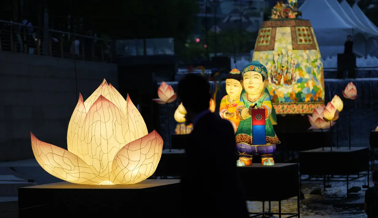 <p>Seorang pengunjung yang mengenakan masker untuk membantu mengekang penyebaran virus corona mengambil foto di dekat lentera yang dipajang untuk merayakan ulang tahun Buddha yang akan datang pada 8 Mei, di aliran umum di Seoul, Korea Selatan, Selasa, 26 April 2022. (AP Photo /Lee Jin-man)</p>